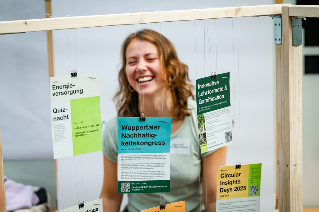 Zu sehen ist der Stand der neuen Effizienz. An einem Holzgestell hängen Karten. Dahinter steht eine Frau und lacht.