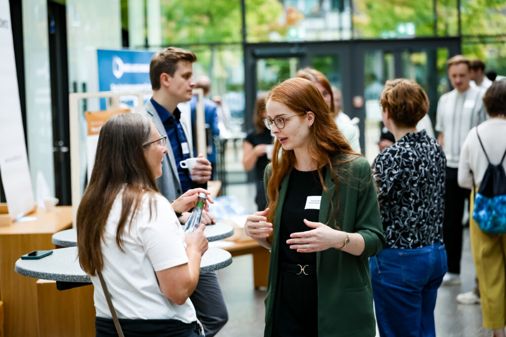 Das Bild zeigt einen Ausschnitt vom Markt der Möglichkeiten auf dem Barcamp. Man sieht Menschen auf einem hellen offenen Gang, die angeregt ins Gespräch vertieft sind.