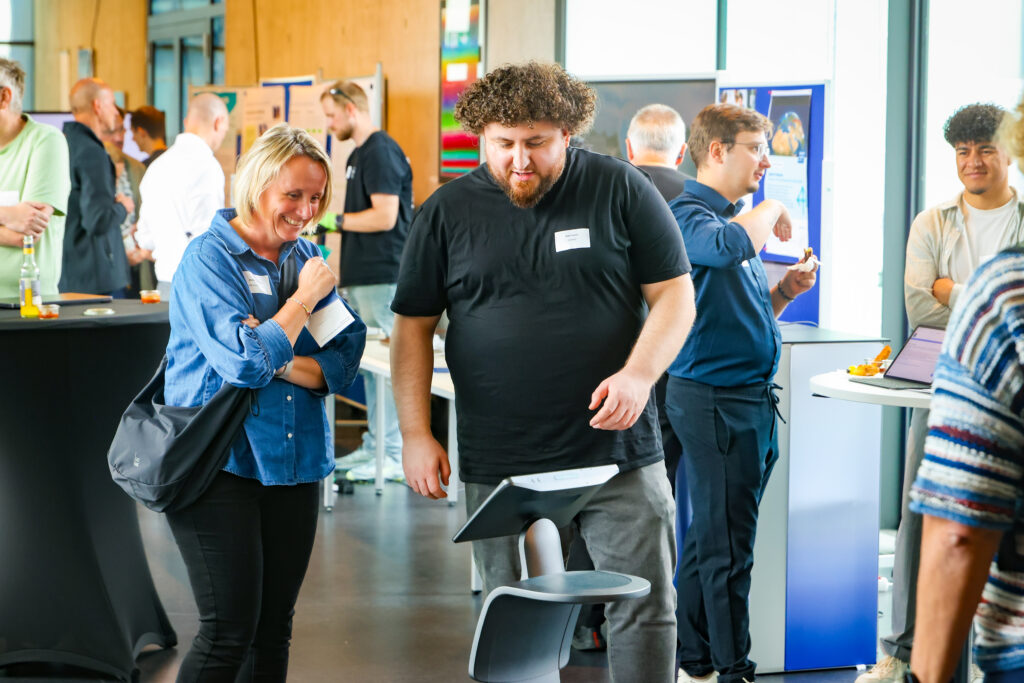 Zwei menschen interagieren mit einem Roboter. Sie stehen in einem Flur eines modernen Gebäudes, im Rahmen einer Messe ähnlichen Veranstaltung
